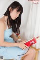 A woman in a blue dress sitting on a chair holding a red phone.