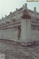 A naked woman standing on top of a stone wall.