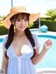 A woman in a blue dress and a straw hat posing by a pool.