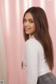 A woman with long brown hair standing in front of a pink curtain.