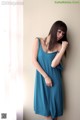 A woman in a blue dress leaning against a wall.