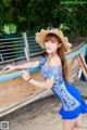 A woman in a blue dress and a straw hat leaning against a boat.