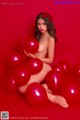 A naked woman sitting on a pile of red balloons.