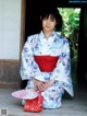 A woman in a blue and red kimono sitting on the ground.