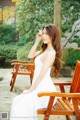 A woman in a white dress sitting on a wooden chair.