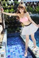 A woman in a pink top and white skirt posing by a pool.