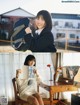 A woman sitting at a desk holding a book and a backpack.