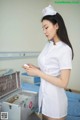 A woman in a white nurse uniform holding a box of medical supplies.