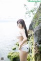 A woman in a white bikini standing on a rock by the water.