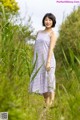 A woman in a purple and white dress standing in tall grass.