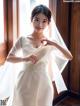 A woman in a wedding dress standing by a window.