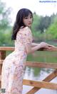 A woman in a floral dress leaning on a wooden fence.