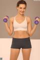 A woman in a white sports bra top and black shorts holding two purple dumbbells.