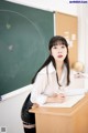 A woman sitting at a desk in front of a blackboard.