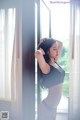 A woman in a black bra and panties standing by a window.